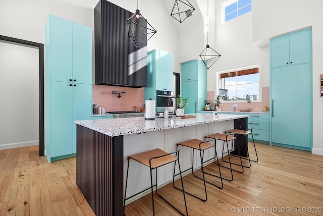 kitchen featuring high vaulted ceiling, light hardwood / wood-style floors, a kitchen island with sink, and blue cabinets