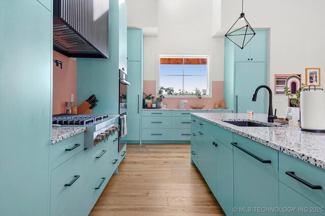 kitchen featuring light hardwood / wood-style floors, blue cabinetry, stainless steel gas cooktop, hanging light fixtures, and sink