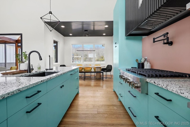 kitchen with extractor fan, decorative light fixtures, stainless steel gas cooktop, light hardwood / wood-style flooring, and sink