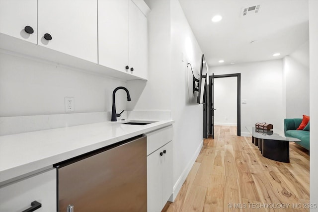 interior space featuring sink, dishwashing machine, white cabinets, and light wood-type flooring