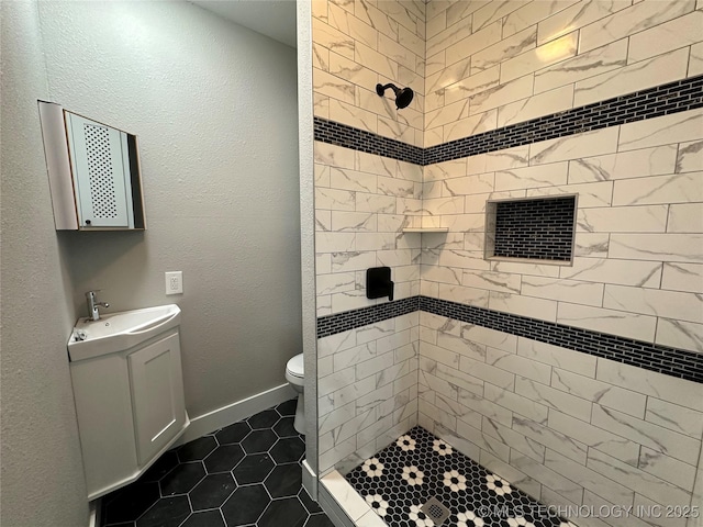 bathroom featuring toilet, a tile shower, tile patterned floors, and sink