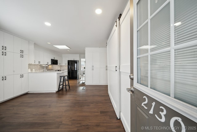 kitchen featuring tasteful backsplash, a barn door, black appliances, a kitchen bar, and white cabinets