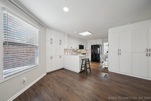 kitchen featuring a kitchen breakfast bar, white cabinetry, a healthy amount of sunlight, and black appliances