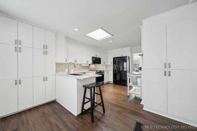 kitchen with black appliances, sink, a skylight, a breakfast bar area, and white cabinets