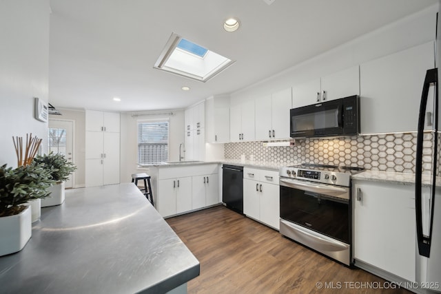 kitchen with a skylight, white cabinetry, kitchen peninsula, black appliances, and sink