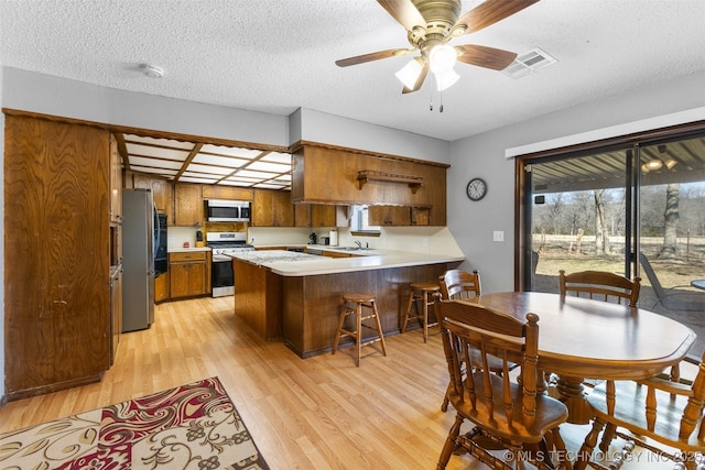 kitchen with a textured ceiling, light wood-type flooring, appliances with stainless steel finishes, kitchen peninsula, and a healthy amount of sunlight