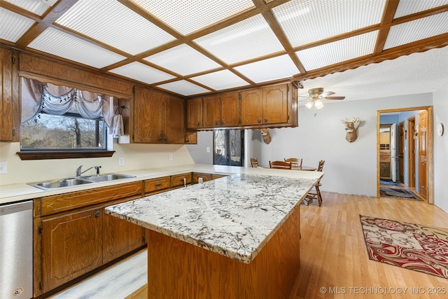 kitchen featuring a kitchen island, sink, stainless steel dishwasher, ceiling fan, and light hardwood / wood-style flooring