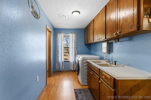 washroom with sink, cabinets, light hardwood / wood-style floors, a textured ceiling, and separate washer and dryer