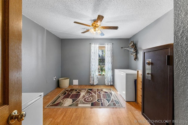 laundry room with ceiling fan, separate washer and dryer, light hardwood / wood-style flooring, and a textured ceiling