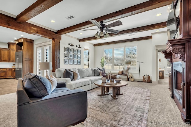 carpeted living room with ceiling fan, a healthy amount of sunlight, and beamed ceiling