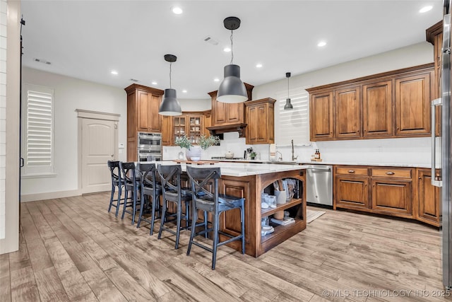 kitchen with stainless steel appliances, light wood-type flooring, hanging light fixtures, a breakfast bar, and a center island