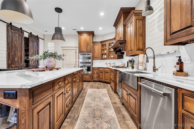 kitchen with a barn door, pendant lighting, light hardwood / wood-style floors, light stone countertops, and stainless steel appliances