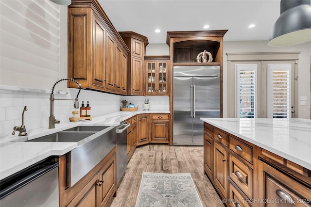 kitchen with stainless steel appliances, light hardwood / wood-style floors, backsplash, and light stone countertops