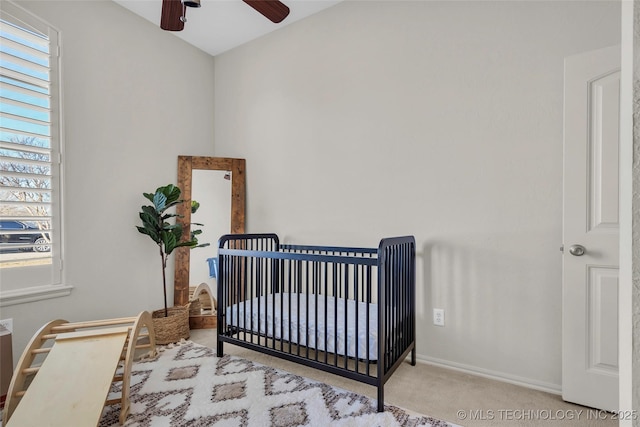 carpeted bedroom with ceiling fan and a nursery area