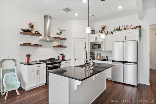 kitchen featuring appliances with stainless steel finishes, wall chimney exhaust hood, white cabinets, sink, and a kitchen island with sink