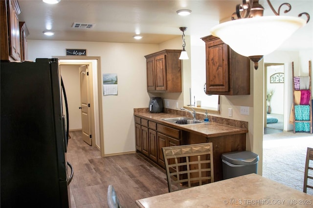 kitchen with black refrigerator, hanging light fixtures, dark hardwood / wood-style floors, and sink