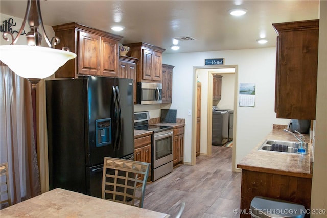 kitchen with washer and clothes dryer, sink, appliances with stainless steel finishes, and light hardwood / wood-style floors