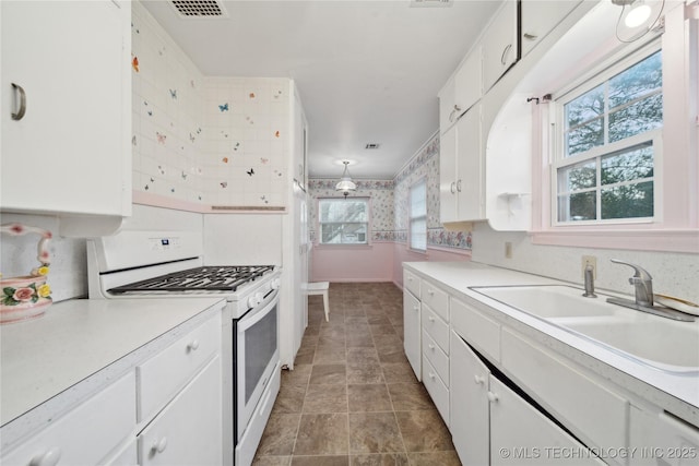 kitchen featuring sink, pendant lighting, white cabinets, and gas range gas stove