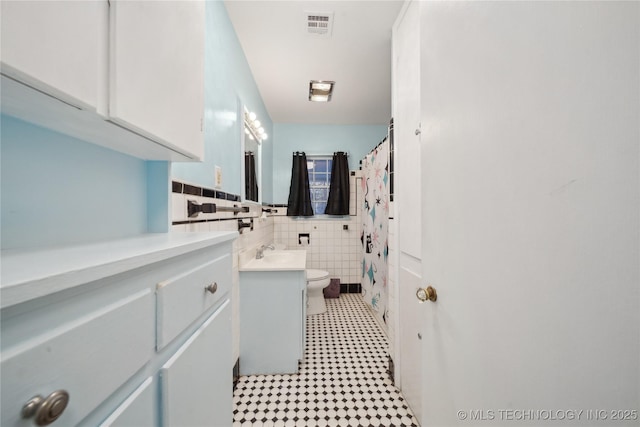 bathroom featuring toilet, tile walls, and vanity