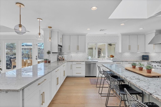 kitchen with appliances with stainless steel finishes, backsplash, white cabinetry, and hanging light fixtures