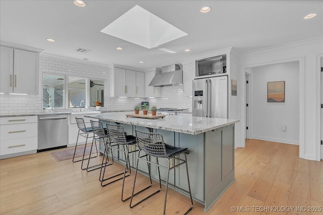 kitchen with appliances with stainless steel finishes, white cabinetry, a kitchen island, and wall chimney range hood