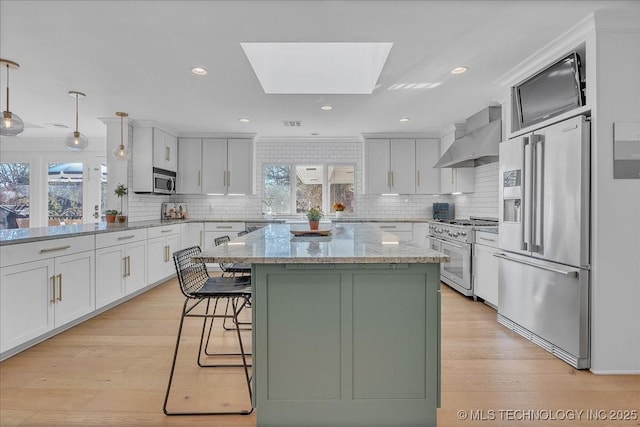 kitchen with wall chimney range hood, pendant lighting, a skylight, light stone countertops, and premium appliances