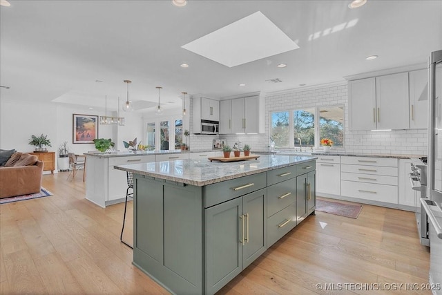 kitchen with white cabinets, a kitchen island, decorative light fixtures, a skylight, and tasteful backsplash