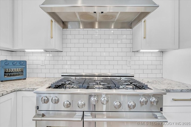 kitchen featuring tasteful backsplash, premium range hood, white cabinetry, stainless steel gas range, and light stone counters