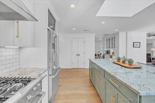 kitchen with stainless steel appliances, tasteful backsplash, wall chimney range hood, crown molding, and light hardwood / wood-style flooring