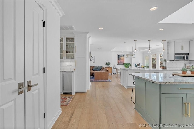 kitchen featuring tasteful backsplash, light wood-type flooring, light stone countertops, pendant lighting, and white cabinets