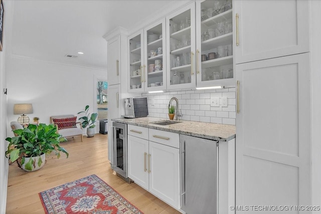 kitchen with beverage cooler, white cabinets, sink, light wood-type flooring, and light stone counters