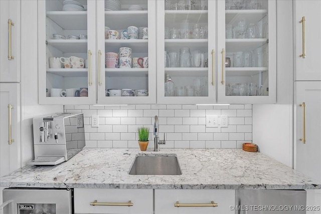 kitchen featuring light stone countertops, sink, backsplash, and white cabinets