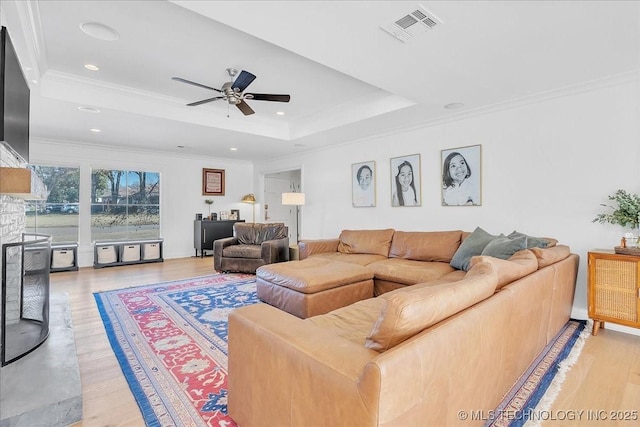 living room featuring a raised ceiling, light wood-type flooring, ornamental molding, and ceiling fan