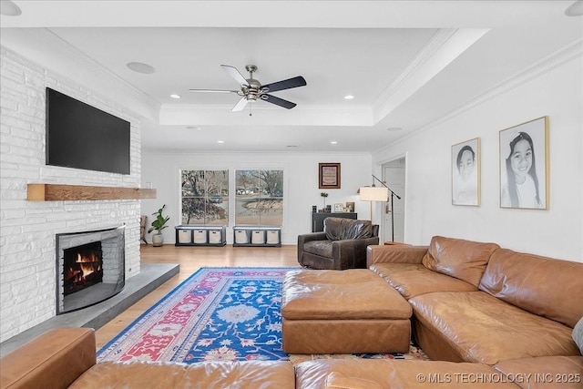 living room with light hardwood / wood-style floors, ceiling fan, a tray ceiling, a fireplace, and crown molding