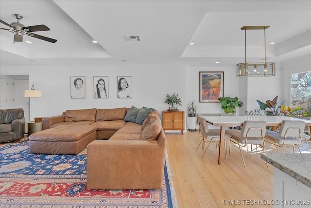 living room featuring ceiling fan, ornamental molding, light hardwood / wood-style flooring, and a raised ceiling