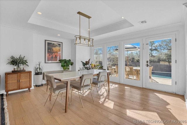 dining room with light wood-type flooring, crown molding, and a raised ceiling