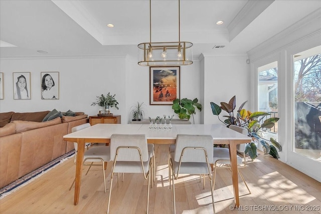 dining room with light wood-type flooring, ornamental molding, and a raised ceiling