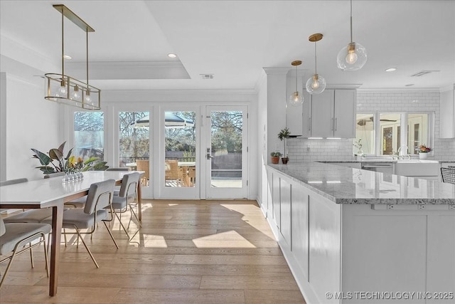 kitchen featuring light stone countertops, white cabinets, decorative light fixtures, decorative backsplash, and light hardwood / wood-style floors