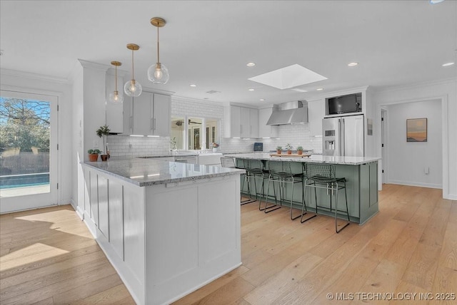 kitchen with pendant lighting, white cabinetry, wall chimney range hood, a skylight, and high end fridge