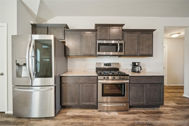 kitchen featuring lofted ceiling, dark hardwood / wood-style floors, dark brown cabinetry, stainless steel appliances, and light stone counters