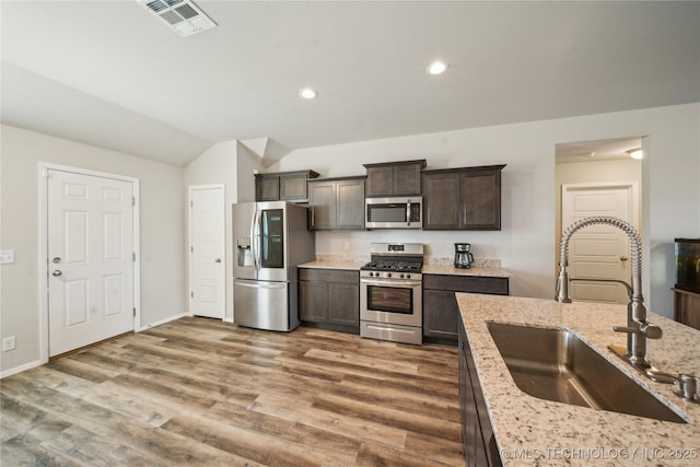 kitchen featuring appliances with stainless steel finishes, dark wood-type flooring, dark brown cabinets, light stone counters, and sink