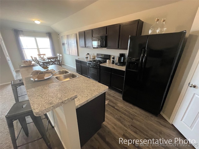 kitchen featuring black appliances, dark hardwood / wood-style flooring, a kitchen breakfast bar, a kitchen island with sink, and vaulted ceiling