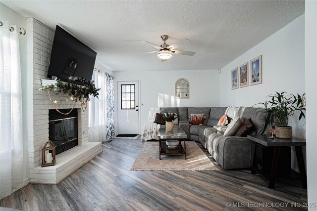 living room featuring ceiling fan, a brick fireplace, a textured ceiling, and hardwood / wood-style floors