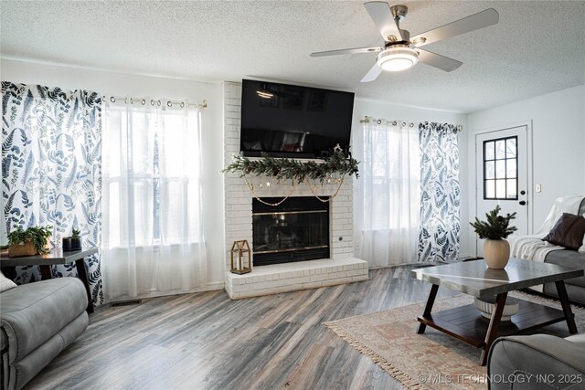 living room featuring ceiling fan, wood-type flooring, a fireplace, and a textured ceiling