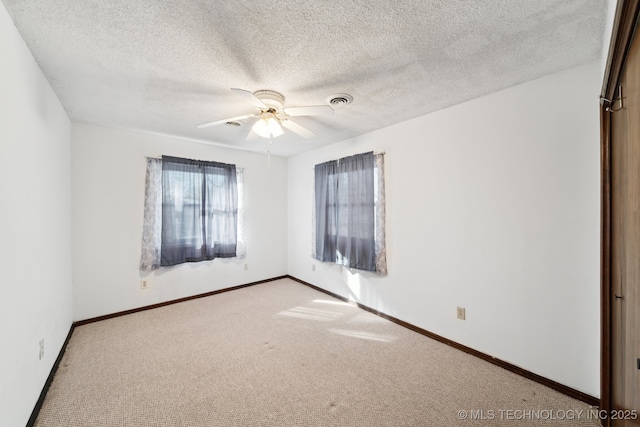 carpeted empty room with visible vents, a textured ceiling, a ceiling fan, and baseboards