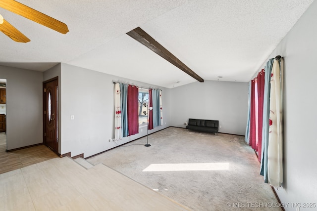carpeted empty room with ceiling fan, vaulted ceiling with beams, baseboards, and a textured ceiling