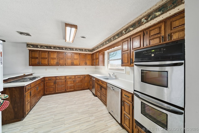 kitchen with visible vents, brown cabinets, appliances with stainless steel finishes, a textured ceiling, and a sink