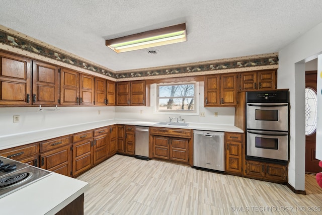 kitchen featuring a sink, a textured ceiling, appliances with stainless steel finishes, and brown cabinetry