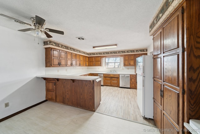 kitchen featuring stainless steel dishwasher, a peninsula, brown cabinetry, and freestanding refrigerator