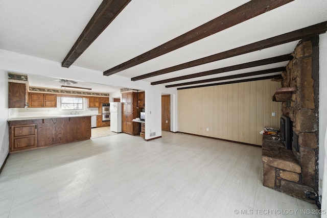unfurnished living room featuring beam ceiling, light floors, wood walls, and a sink